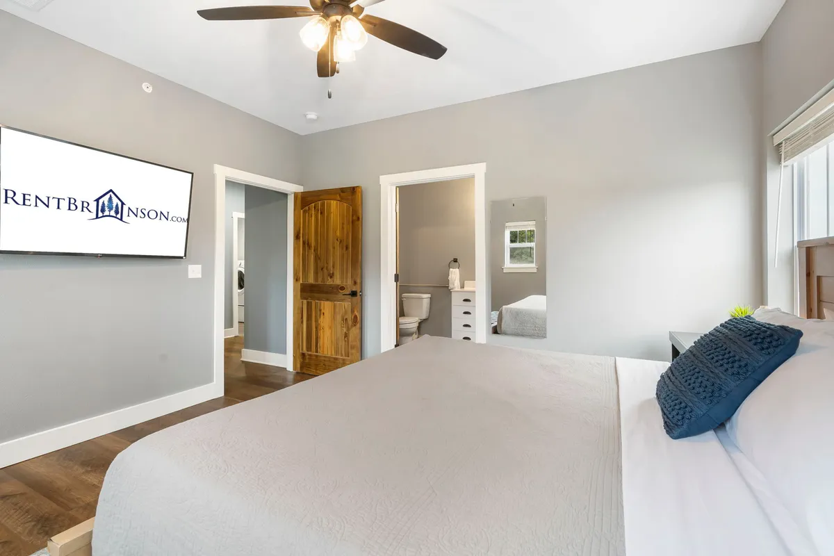 A serene bedroom scene with a comfortable bed, a television mounted for easy viewing, a wooden door for privacy, and a mirror, creating a peaceful and functional space to rest or enjoy some quiet entertainment.