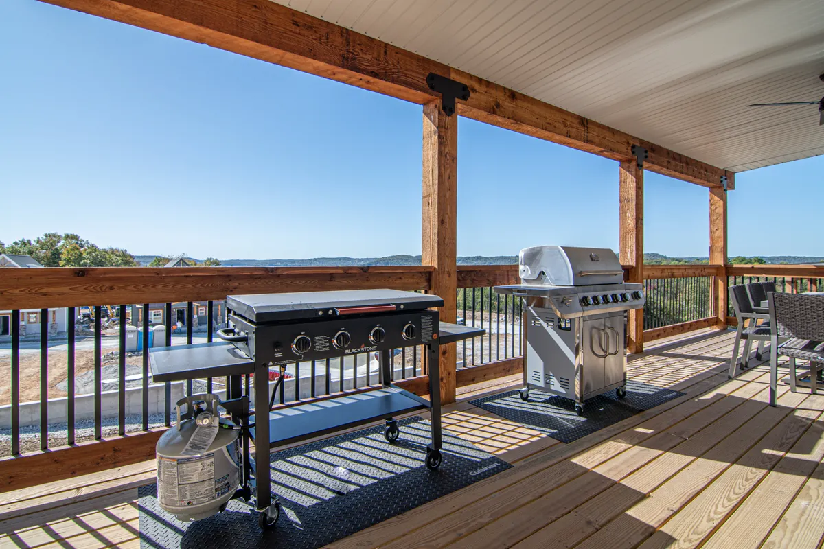 This exterior scene showcases a grill and outdoor seating area overlooking a scenic view. The space is set up for barbecuing and dining outdoors, suggesting a relaxed and social atmosphere ideal for entertaining guests.