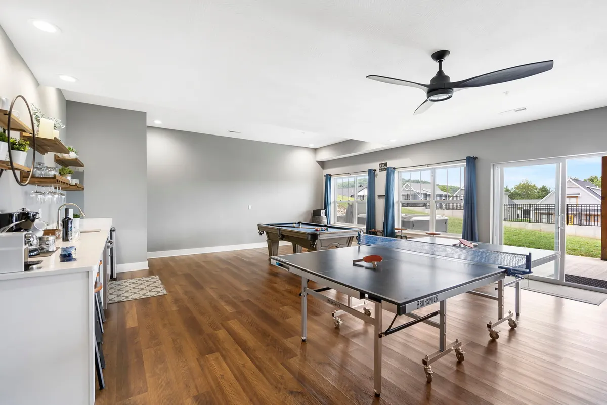 This shot offers a different angle of a similar entertainment space, featuring both a ping pong and a pool table, along with a stylish bar area and more large windows. The room exudes a playful yet relaxed vibe and is ideal for celebrations, casual hangouts, or spirited family tournaments.