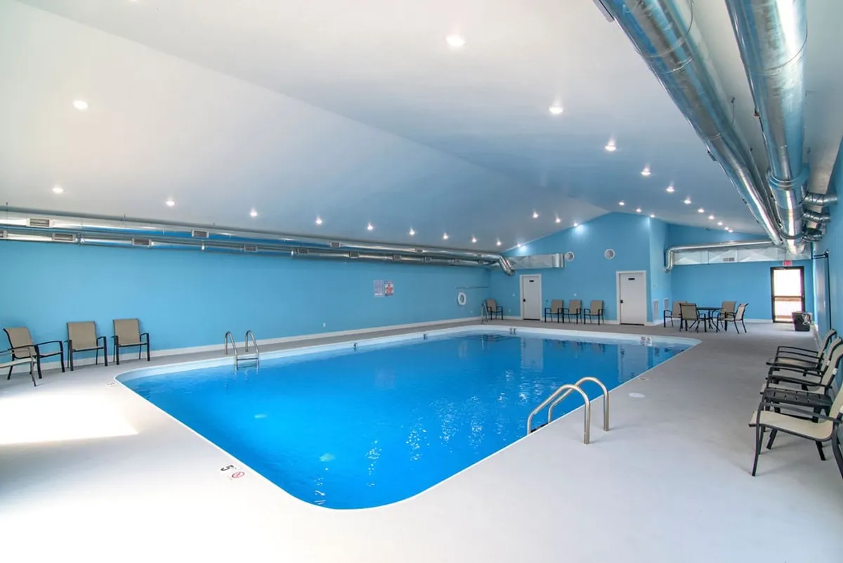 This interior image features a bright indoor swimming pool area with comfortable seating along the side, vibrant blue walls, and large windows letting in natural light. The space feels tranquil and is ready for group swimming, relaxing by the pool, or hosting gatherings even during cooler months.
