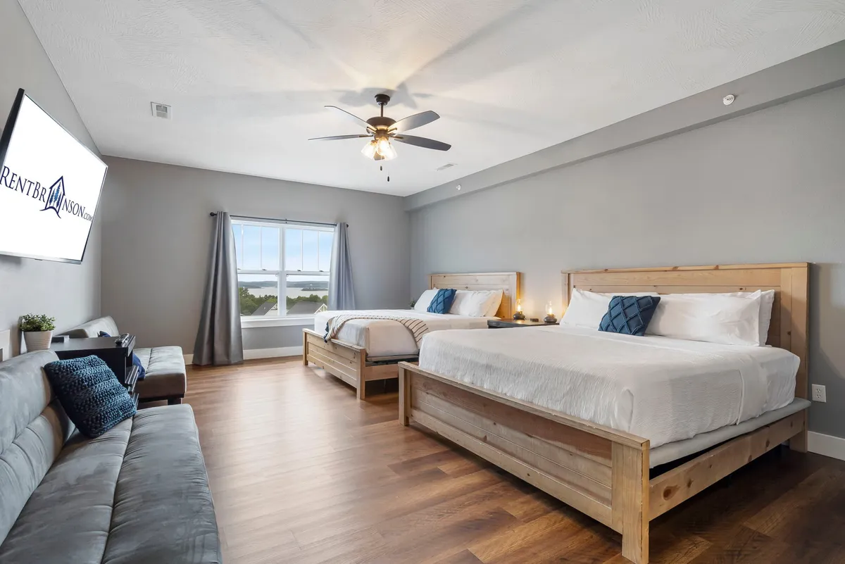 A spacious bedroom with two wooden beds, a sofa for additional seating, a large window letting in natural light, and a TV for entertainment. The setup is ideal for families or friends sharing a room, offering both communal and private relaxation spaces.