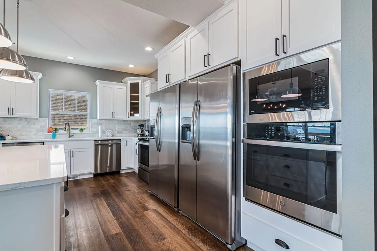 A modern kitchen with stainless steel appliances, white cabinetry, and warm wooden flooring. The space is set up for cooking and entertaining, with an emphasis on culinary tools and a family-friendly, functional layout. It evokes the idea of preparing group meals, from pancake breakfasts to gourmet feasts.
