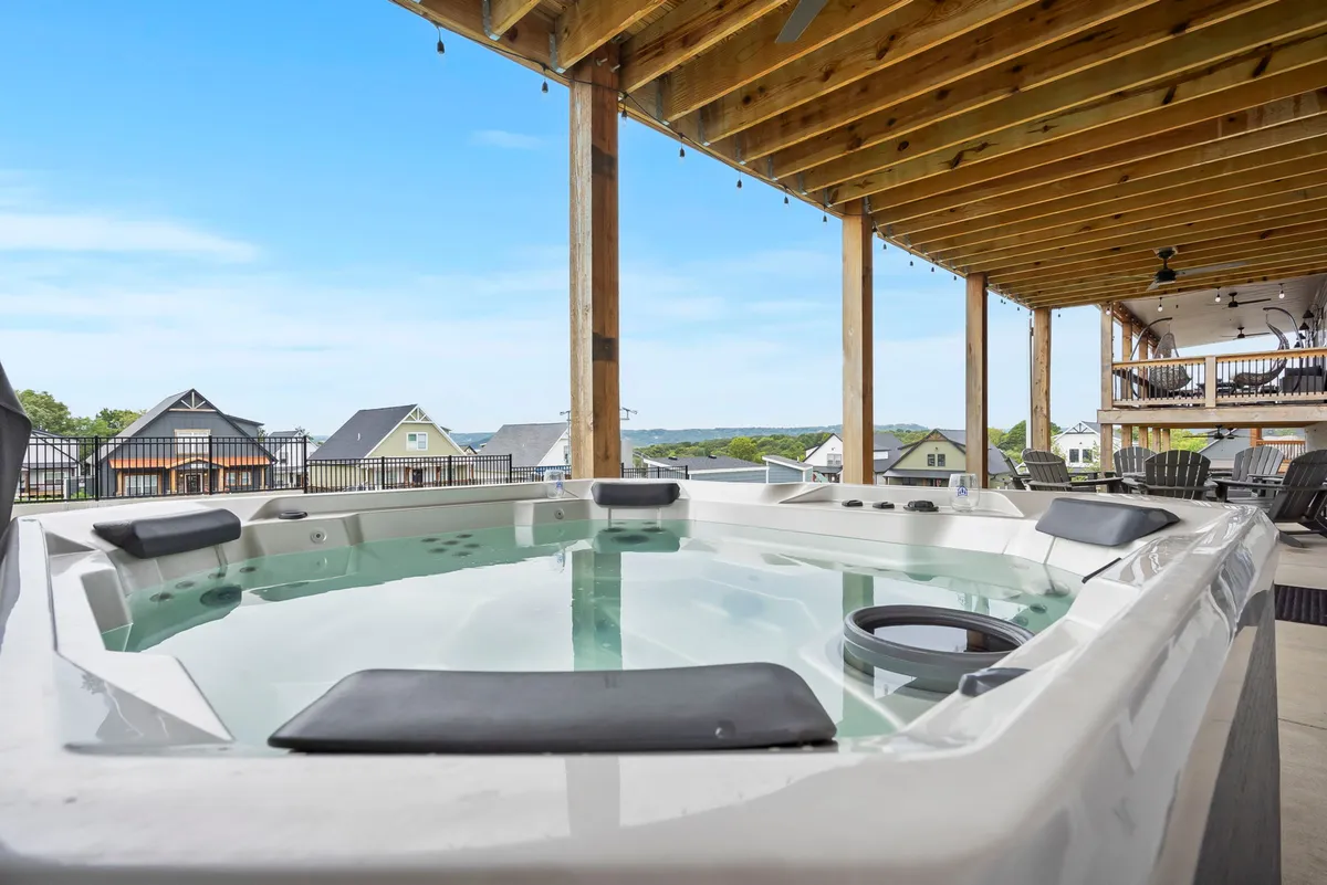 This image features an inviting outdoor hot tub set against a backdrop of surrounding houses and robust wooden beams. Guests are seen relaxing in the hot tub and socializing with friends, with the soft glow of sunset adding a tranquil and celebratory mood to the scene.