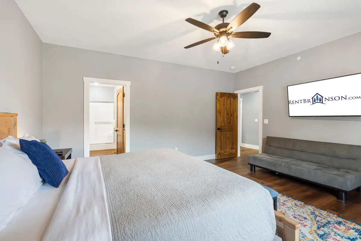 A welcoming bedroom with a bed, sofa, and TV, flanked by doorways leading to the rest of the home. The design is both cozy and accessible, providing a versatile space for relaxing, watching TV, or hosting a small get-together.