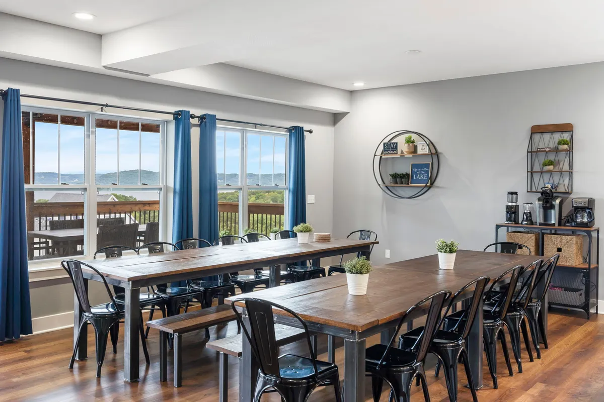 A long wooden dining table sits before large windows that offer breathtaking views of the lake. The table is styled for a group, with ample seating and tasteful décor that hints at celebration dinners or casual breakfasts. Natural light fills the room, creating a welcoming social atmosphere.