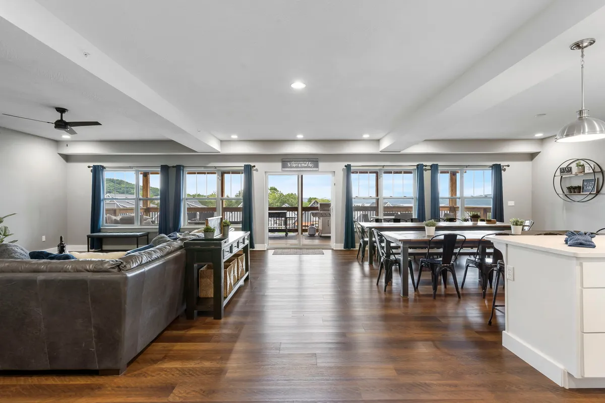 A spacious living area flows into a dining space, all illuminated by large windows that frame scenic views. Comfortable seating invites relaxation, while the set dining table is ready for a meal or game night. The cozy, inviting atmosphere is perfect for either intimate gatherings or larger celebrations.