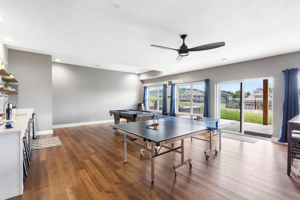 This interior image focuses on a ping pong table and pool table in a spacious room with large windows and an adjacent kitchen area. The setup is ideal for friendly competitions, celebrations, and socializing, blending recreation with comfort and convenience.