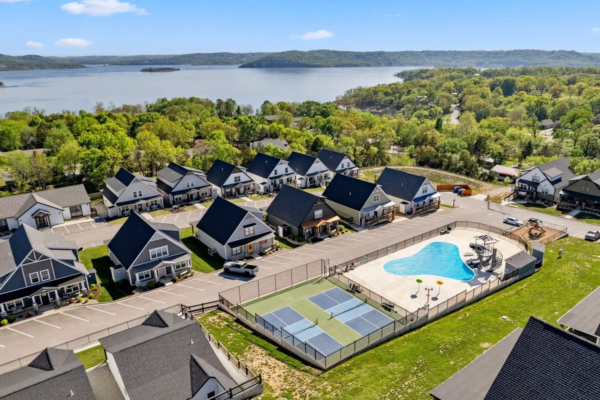 This exterior image captures the community swimming pool, tennis courts, townhouses, and a sweeping lake view in the background. The setting is bright and inviting, with clear signs of group activities like swimming, playing tennis, socializing by the pool, and relaxing outdoors. The lakeside and sunset ambiance are visible, making it feel ideal for summer fun or outdoor gatherings.