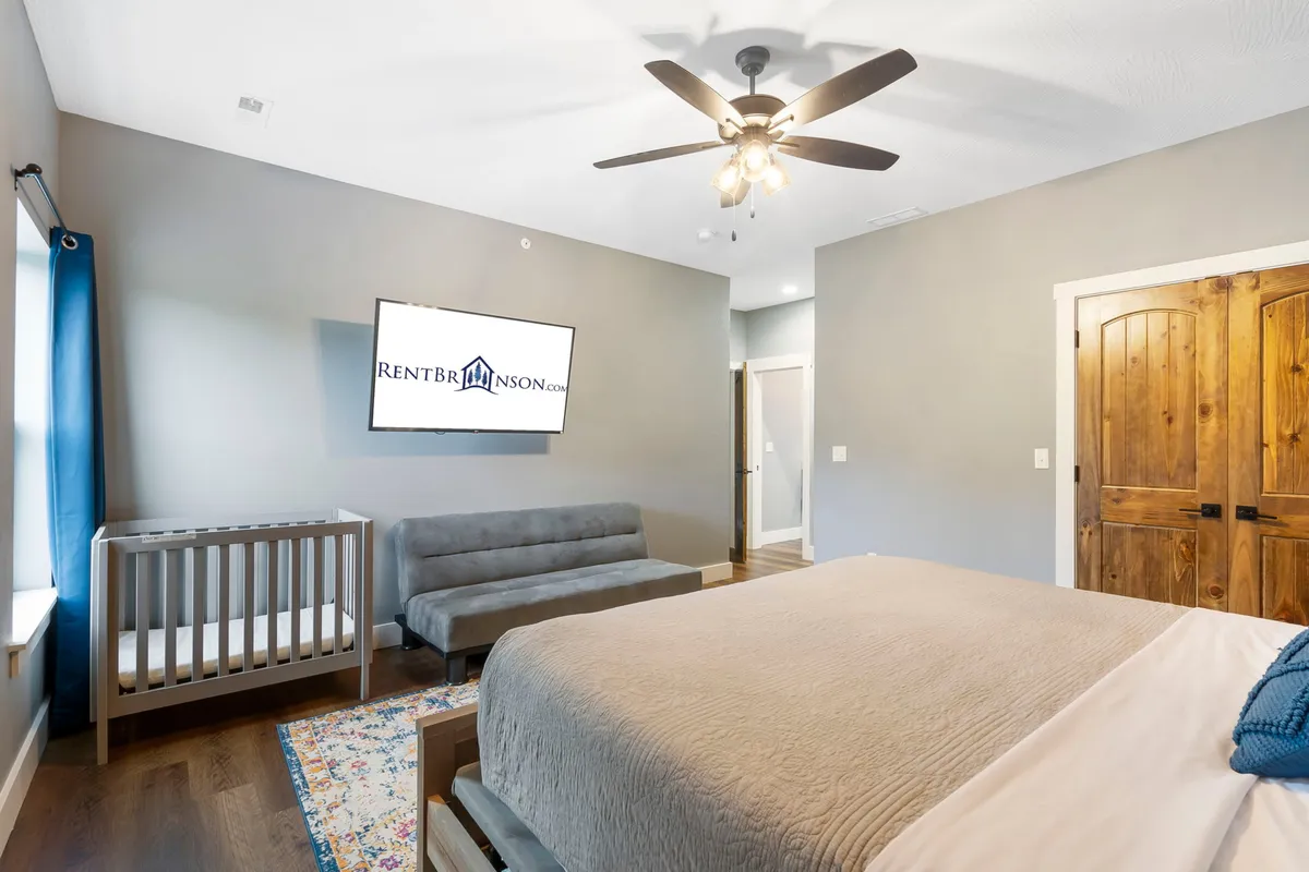 A cozy bedroom featuring a comfortable bed, a sofa for lounging, a TV for entertainment, and a mini-crib beside the bed, ideal for families with small children. The space is inviting, with soft lighting and practical furnishings that cater to both relaxation and family needs.