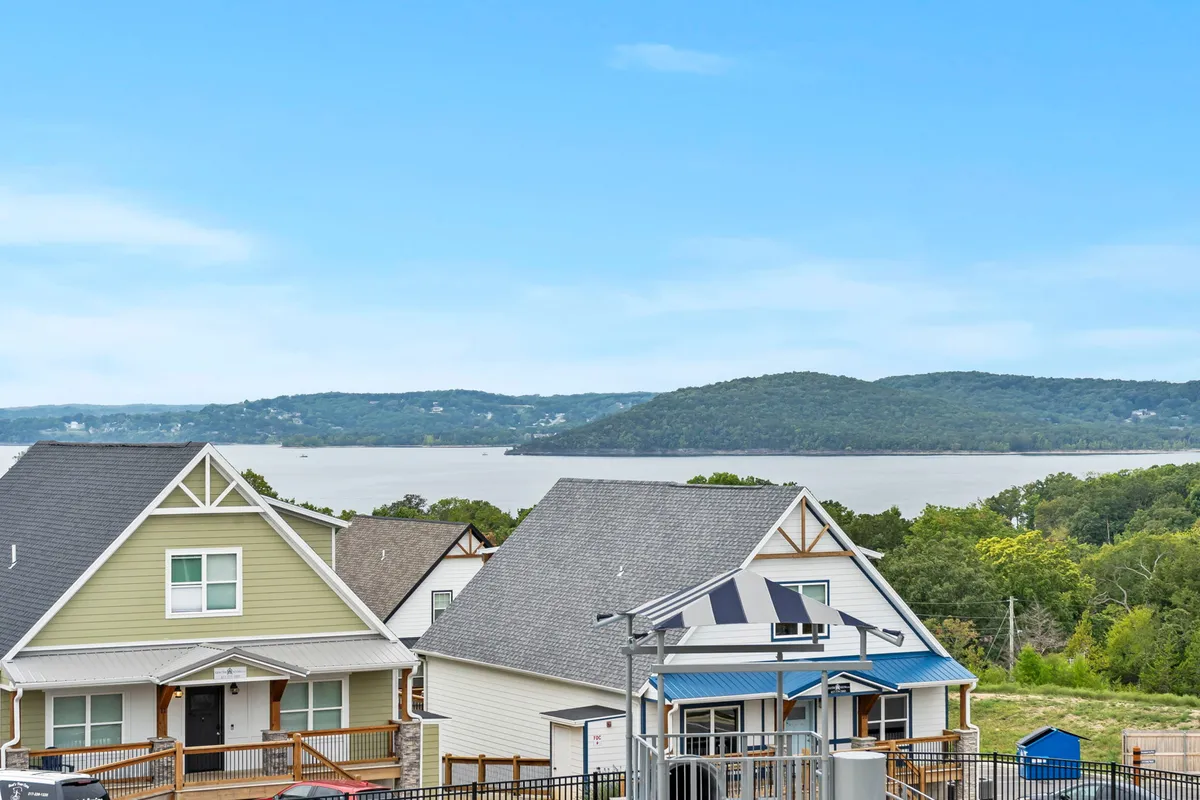 This image offers a sweeping view of Table Rock Lake, with the tranquil water framed by houses, mountains in the background, and an expansive sky above. The scene hints at outdoor activities like boating, fishing, and lakeside relaxation, encapsulating the allure of lakeside living.